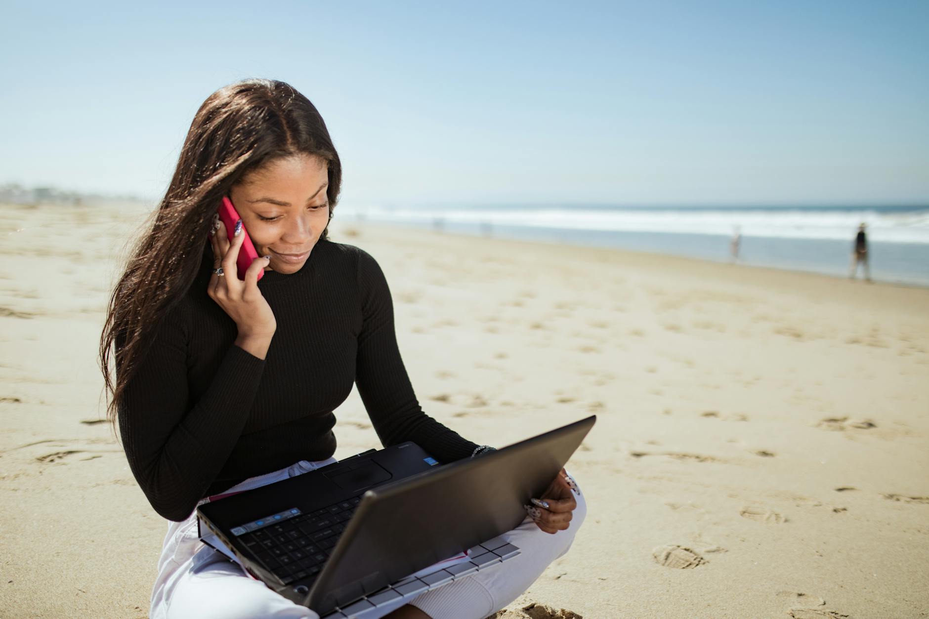 a woman in black long sleeve shirt using laptop computer on beach
